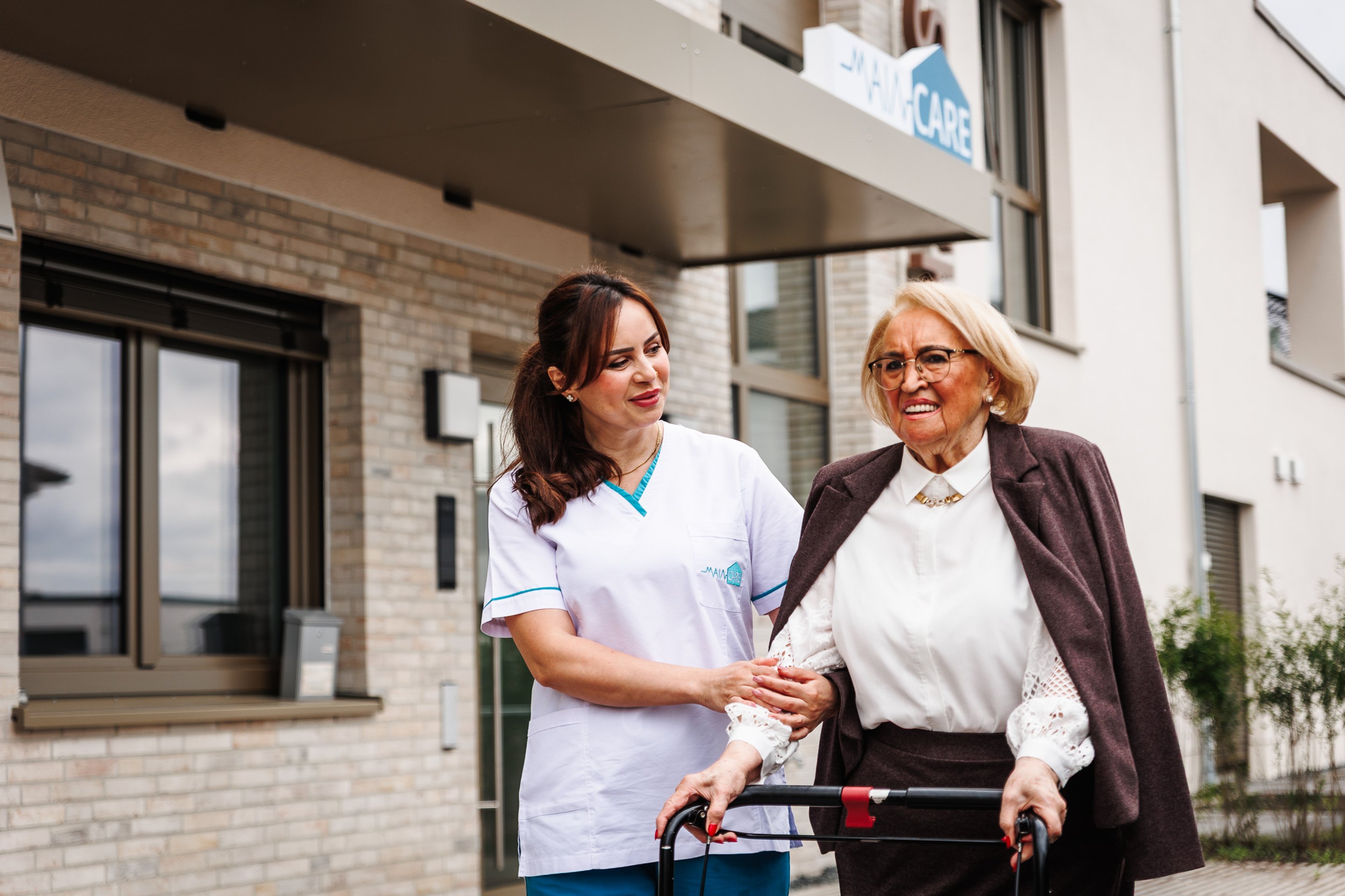 Main Care Pflegefachkraft begleitet eine Seniorin mit Rollator am Standort Erlensee
