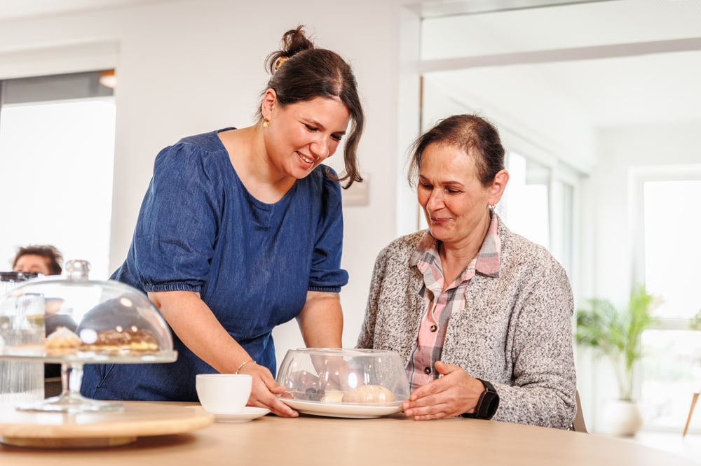 Pflegefachkraft unterstützt eine Seniorin beim gemeinsamen Essen